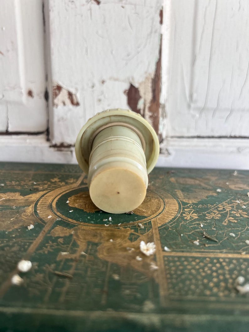 Puede incluir: Un tap&oacute;n de botella vintage en beige claro y blanquecino. El cuerpo cil&iacute;ndrico y la parte superior circular sugieren que est&aacute; hecho de pl&aacute;stico o un material similar. El dise&ntilde;o es simple y funcional, para sellar botellas.