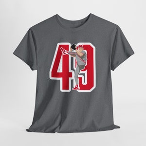 Peut inclure: Un t-shirt gris foncé chiné avec un numéro 49 rouge et blanc sur le devant. Un joueur de baseball est représenté dans le numéro 49, portant une casquette rouge et un uniforme blanc.