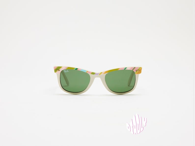 May include: Off-white sunglasses with green lenses and colorful patterned frames. The frames feature a mix of pink, green, and yellow hues. The sunglasses have a classic, rectangular shape and are set against a white background.