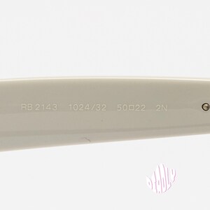 May include: Close-up of the arm of a pair of off-white sunglasses. The text "RB 2143 1024/32 50☐22 2N" is printed on the arm. The hinge and a small circular detail are visible.