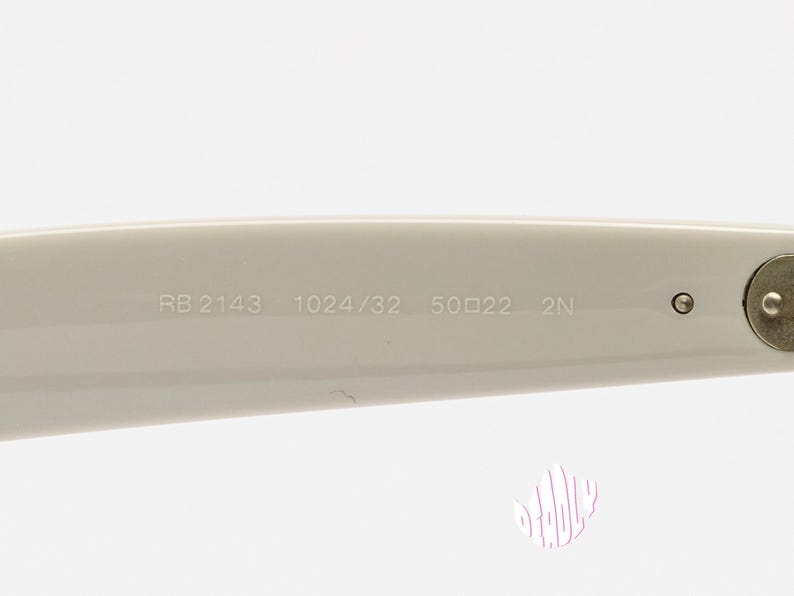 May include: Close-up of the arm of a pair of off-white sunglasses. The text "RB 2143 1024/32 50☐22 2N" is printed on the arm. The hinge and a small circular detail are visible.