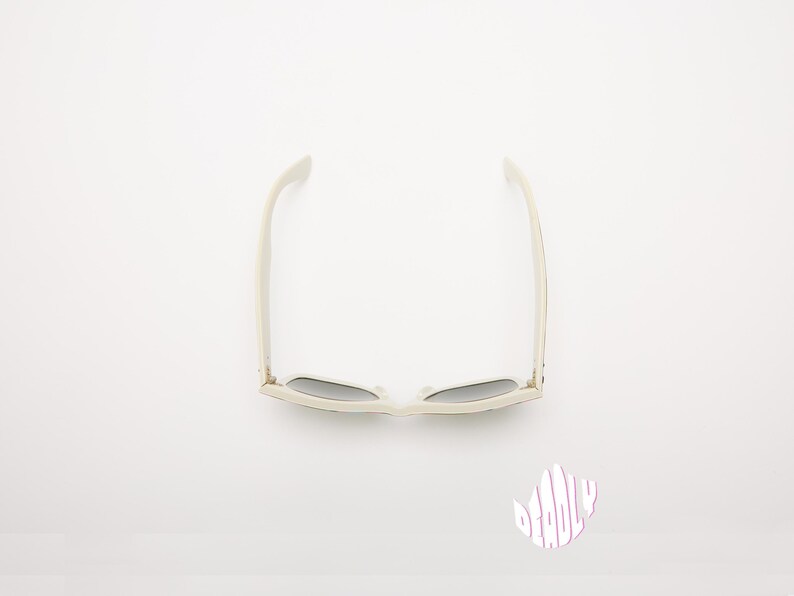 May include: Off-white sunglasses with dark lenses, viewed from above. The sunglasses have a classic rectangular frame and are set against a white background. The image also includes a small, stylized graphic with the word "DEADLY".