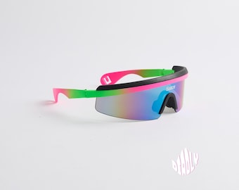 Puede incluir: Un par de gafas de sol rosa, verde y negro con lentes espejados. Las gafas tienen un diseño futurista y dicen "Slayce" en el lateral.