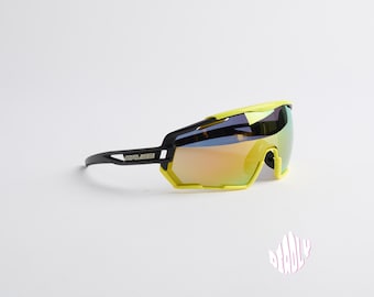 Puede incluir: Gafas de sol de ciclismo amarillas y negras con lente espejada. Las gafas tienen un diseño deportivo y son ideales para actividades al aire libre.