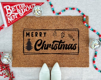 May include: A rectangular coir doormat with the words "MERRY Christmas" in black script and a Christmas tree illustration. A red pennant with white text and a disco ball are on the left. A colorful garland and disco ball are on the right.