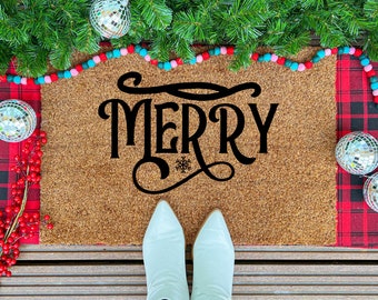 May include: A festive doormat made of brown coir, featuring the word "MERRY" in black script with a snowflake detail. The scene includes a red tartan runner, disco balls, and evergreen boughs, creating a Christmas theme.