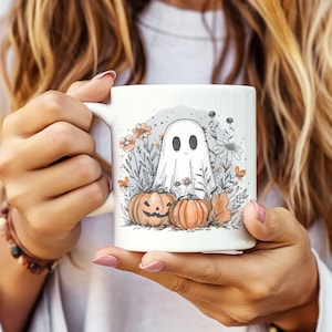 May include: White ceramic mug featuring a Halloween-themed design. The illustration includes a friendly ghost, pumpkins, flowers, and foliage. The mug is held by a person.