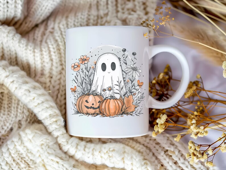 May include: White ceramic mug featuring a Halloween-themed illustration. The design includes a friendly ghost, two pumpkins, flowers, and foliage. The mug has a curved handle and is set against a cozy, textured background.