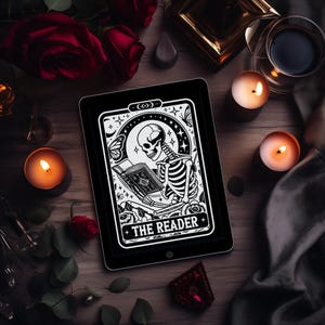以下が含まれることがあります： 黒いタブレットには、「THE READER」のテキストが入った、本を読む骸骨のタロットカードのイラストが表示されています。 この画像は、ろうそく、赤いバラ、暗い布に囲まれ、神秘的な雰囲気を醸し出しています。