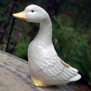 Könnte beinhalten: Weiße Keramik-Gänse-Pflanzer mit gelbem Schnabel und Füßen. Die Gans hat einen ausgehöhlten Rücken zum Pflanzen.