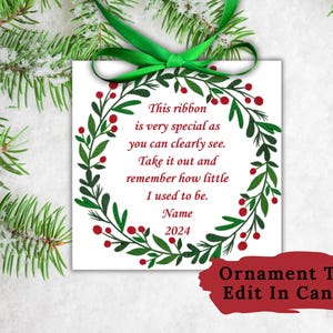 Puede incluir: Una etiqueta de adorno blanca con una corona verde y bayas rojas. La etiqueta tiene el texto "Esta cinta es muy especial como puedes ver claramente. Sácala y recuerda lo pequeño que era. Nombre 2024". La etiqueta está etiquetada como "Ornament Tag Edit In Canva".