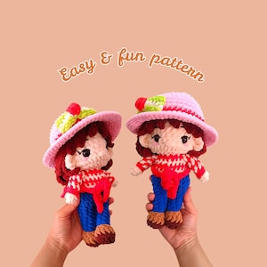 May include: Two handmade crochet dolls, each wearing a pink hat with a green and red accent, red and white sweater, blue jeans, and brown shoes. The dolls have brown hair and are held up against a peach background. Text in the image reads "Easy & fun pattern."
