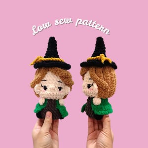 May include: Two crochet witch dolls with brown hair, black hats, and green capes are displayed against a pink background. The dolls have a light skin tone and are wearing black hats with yellow trim. The text "Low sew pattern" is written above the dolls.