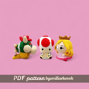 May include: Crocheted figures of Bowser, Toad, and Princess Peach, set against a pink background. Bowser is green, white, and yellow. Toad is white, red, and blue. Princess Peach is yellow and pink. The text "PDF pattern byemiliartwork" is at the bottom.