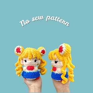 May include: Two handmade crochet dolls, featuring yellow hair, red accents, and blue and white outfits. The dolls are held up against a light blue background. The text "No sew pattern" is written in white cursive above the dolls.