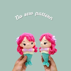 Pode incluir: Duas bonecas de sereia de crochê com cabelo rosa, pele clara e caudas turquesas. As bonecas têm uma parte superior lilás clara e amarela. O texto "No sew pattern" está escrito em itálico branco acima das bonecas.