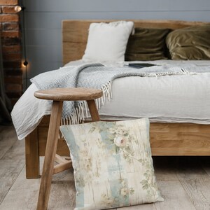May include: A wooden stool with a floral patterned pillow sitting in front of a bed with a white blanket and green pillows.