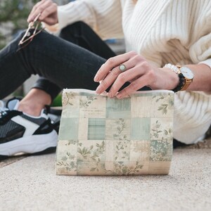May include: A small, rectangular zippered pouch with a patchwork design featuring floral and geometric patterns in shades of beige, green, and white.