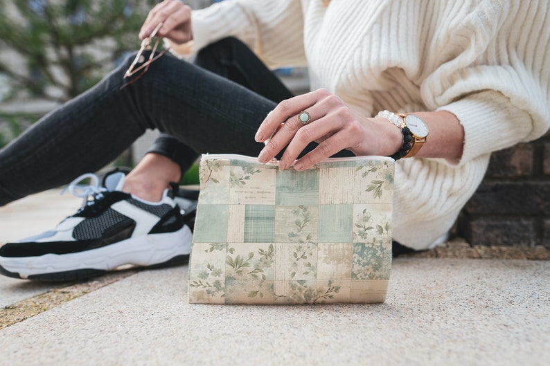 May include: A small, rectangular zippered pouch with a patchwork design featuring floral and geometric patterns in shades of beige, green, and white.