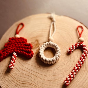 May include: Three handmade Christmas ornaments: a red and white candy cane, a red Christmas tree, and a white wreath.