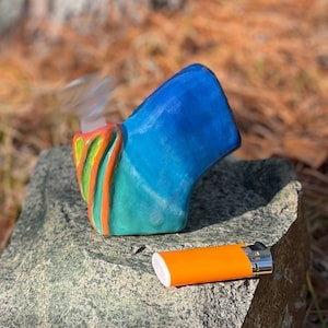 May include: A blue, green, and orange ceramic pipe with a lighter next to it.