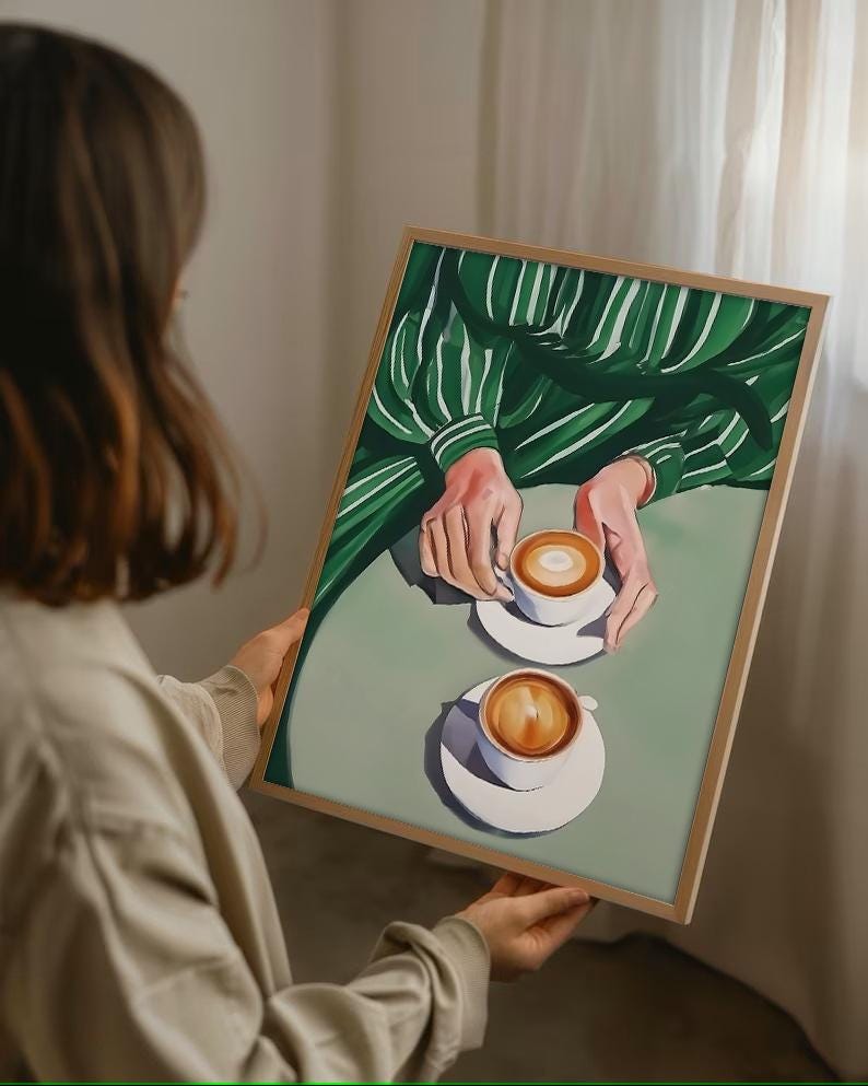 May include: A painting of two cups of coffee on a green and white striped tablecloth. The cups are white with brown coffee and a layer of foam on top. The painting is framed in a light wood frame.