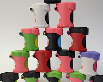 May include: A stack of 15 colorful, cylindrical containers with a unique design. Each container has a different color combination, including pink, green, red, black, and white. The containers have a small, round opening on the top and a label that reads "BENTOBLAZE.COM".