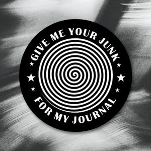 May include: A black and white round sticker with the text "GIVE ME YOUR JUNK FOR MY JOURNAL" encircling a white spiral design. The sticker has four white stars. The background is a blurred grayscale.