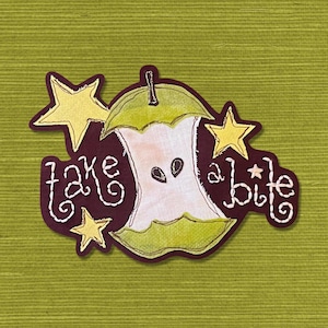 May include: A brown felt patch with the text "take a bite" in white stitching. A green apple core with seeds is in the center of the patch. Three yellow stars are around the apple core.