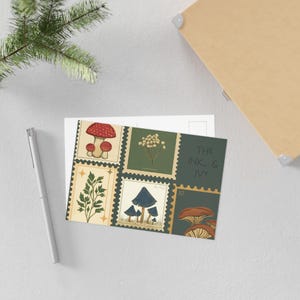 May include: A rectangular postcard featuring a grid of six postage stamp designs. The illustrations include red mushrooms, white flowers, green foliage, blue mushrooms, and brown mushrooms. The text THE INK & IVY and the number 52 are printed on the right.