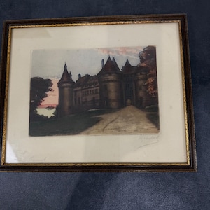 May include: A framed print depicting a stone castle with multiple towers and a central arched entrance, set against a soft pink and blue sky. The artwork is enclosed in a dark brown wooden frame with a thin gold inner border and a cream mat.
