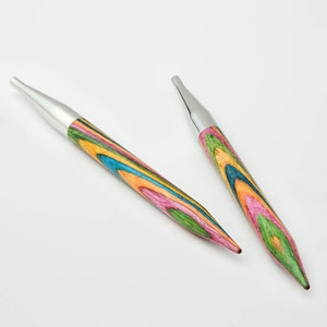 May include: Two knitting needles with a colorful, striped wooden shaft and a silver metal tip. The needles are angled towards each other against a white background. The wood grain features shades of pink, green, blue, and orange.