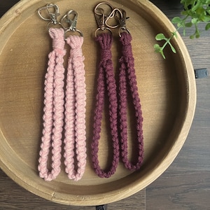 May include: Two keychains with metal clasps. One keychain is pink and the other is burgundy. Both keychains are made of braided cord.