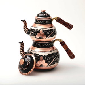 May include: A traditional Turkish double-spout teapot with a black and copper finish. The teapot has intricate floral and geometric designs and wooden handles.