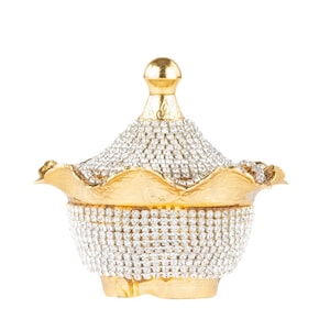 May include: A gold decorative bowl with a lid, covered in clear rhinestones. The bowl has a scalloped edge and a decorative design on the lid.