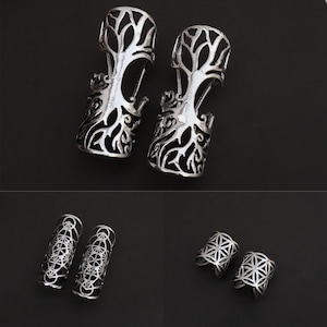 May include: Silver-toned metal finger armor rings with intricate tree and geometric designs. The rings feature openwork patterns, including a tree of life and sacred geometry symbols. The jewelry is displayed on a black background.