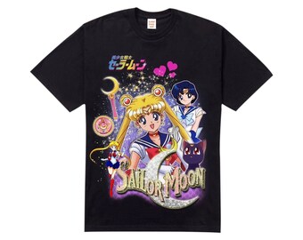 Könnte beinhalten: Schwarzes T-Shirt mit einem Grafikdruck von Sailor Moon und anderen Charakteren aus der Anime-Serie. Der Text "美少女戦士セーラームーン" ist auf dem Shirt gedruckt.