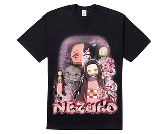 Könnte beinhalten: Schwarzes T-Shirt mit einem Grafikdruck von Anime-Charakteren aus der Serie "Demon Slayer". Die Charaktere sind Nezuko Kamado, Tanjiro Kamado und Zenitsu Agatsuma. Der Text "Nezuko" ist in einer Graffiti-Schriftart geschrieben.