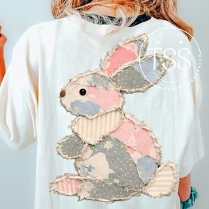 May include: White t-shirt featuring a patchwork bunny design in pink, blue, and gray. The bunny has a distressed, vintage look. The shirt is a casual, everyday wear item.