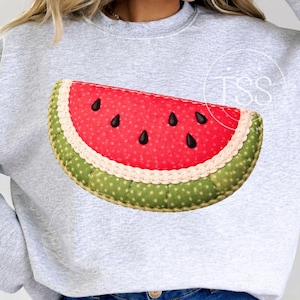 May include: A light gray sweatshirt featuring a large, appliqued watermelon slice. The watermelon has a red center with black seeds, a white rind, and a green, dotted outer edge. The design is centered on the front of the sweatshirt.