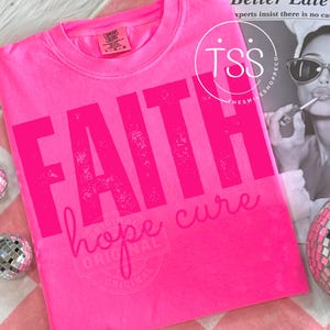 Puede incluir: Camiseta rosa brillante Comfort Colors con las palabras "FAITH", "hope" y "cure" impresas en rosa oscuro. La camiseta tiene cuello redondo y mangas cortas. La palabra "ORIGINAL" también está impresa en la camiseta.