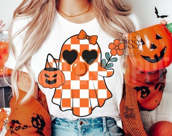 May include: A white t-shirt featuring a checkered ghost wearing heart-shaped sunglasses and a bow. The ghost is holding a small orange pumpkin with a jack-o'-lantern face.