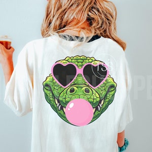 May include: A white t-shirt with a green alligator wearing pink heart-shaped sunglasses and blowing a pink bubble.