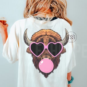 May include: A white t-shirt with a brown and white bison wearing pink heart-shaped sunglasses and blowing a pink bubble.