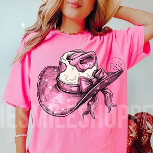 May include: Pink t-shirt featuring a pink and white cowgirl hat graphic with stars and a bow. The text "TSS" is on the shirt.