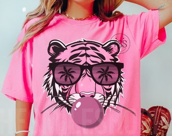 May include: Pink t-shirt with a graphic of a tiger wearing sunglasses and blowing a bubble. The sunglasses have palm trees reflected in them.