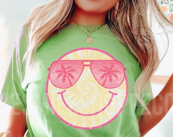 Puede incluir: Camiseta verde con una cara sonriente tie-dye que lleva gafas de sol rosas con palmeras reflejadas en las lentes.