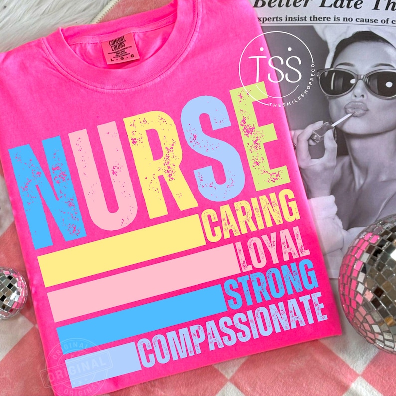 Op de afbeelding: Een felroze t-shirt met het woord "NURSE" in grote, kleurrijke letters. Daaronder staan de woorden "CARING, LOYAL, STRONG, COMPASSIONATE" in een bijpassend lettertype. Het shirt is van het merk Comfort Colors.