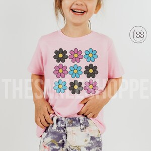 May include: A pink t-shirt with a graphic of nine colorful daisies. The daisies are arranged in a 3x3 grid pattern. The daisies are black, pink, blue, and light blue.