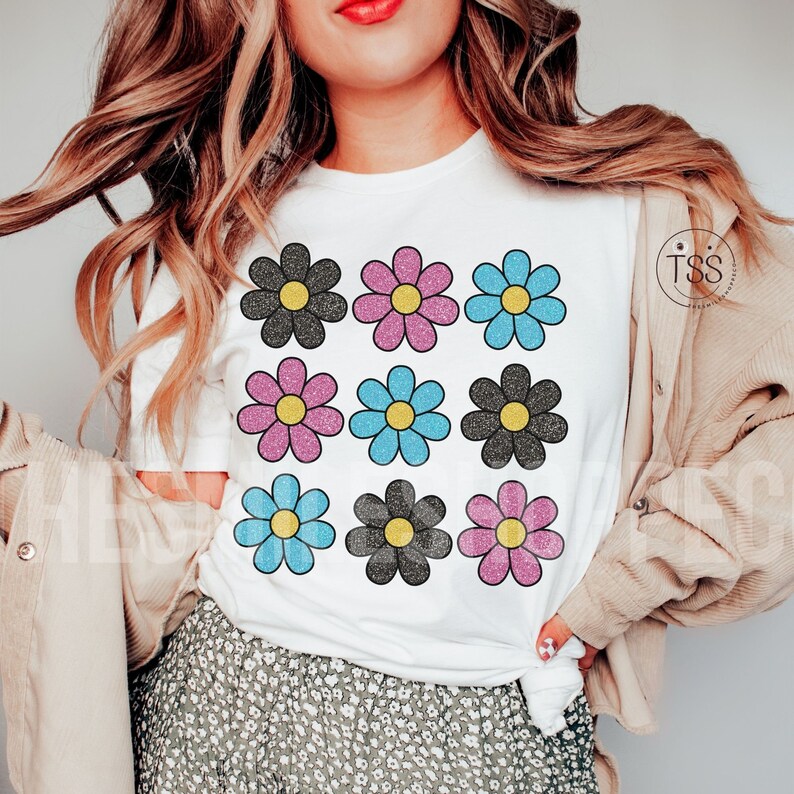 May include: White t-shirt with a pattern of nine colorful daisy flowers. The flowers are black, pink, and blue with glitter accents.